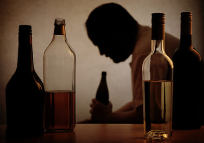 бутылки с алкоголем на фоне пьющего мужчины